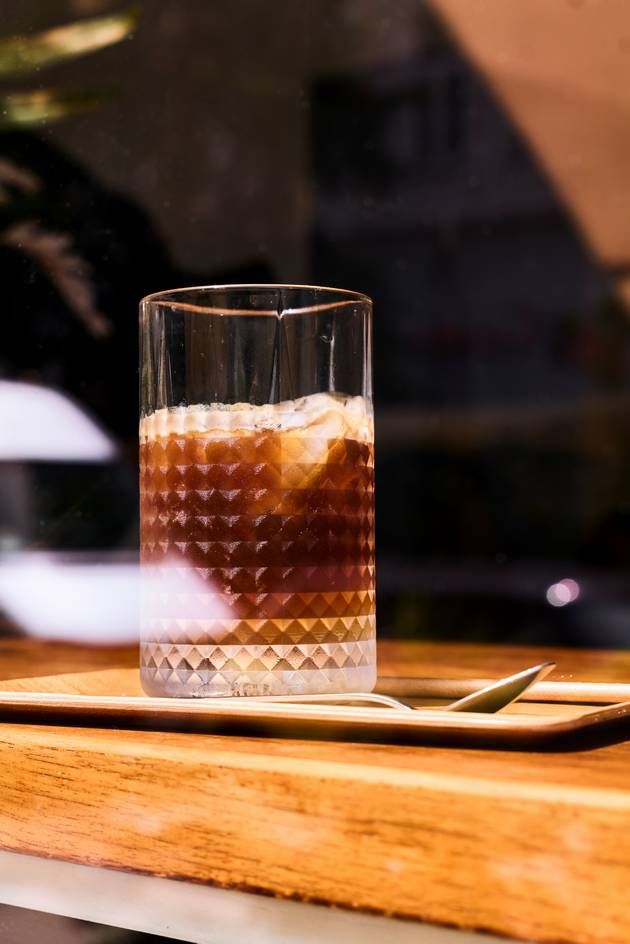 A glass of espresso tonic placed on a wooden table, highlighting its deep hue and the warmth of the surrounding ambiance.