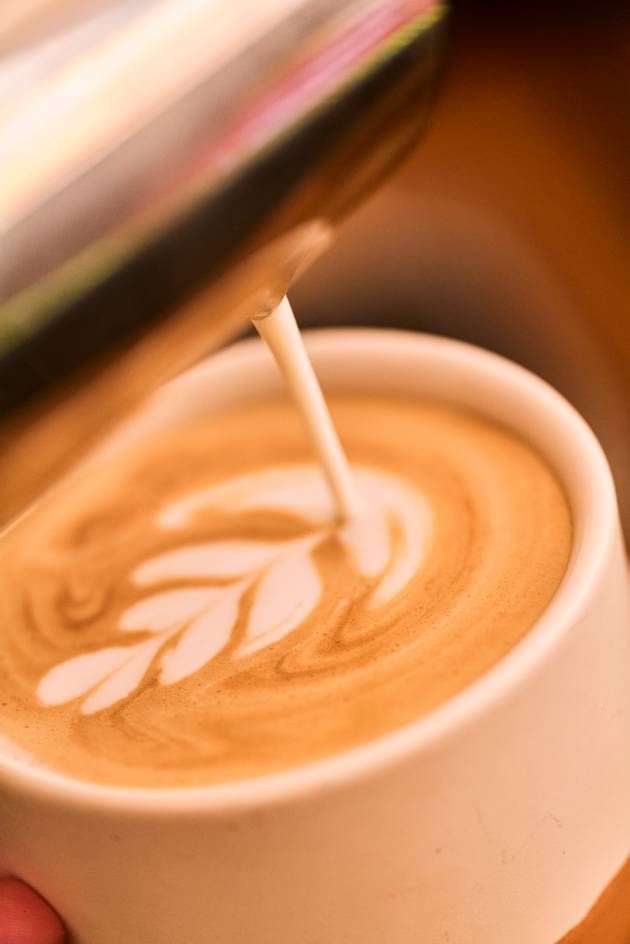 Milk is being poured into a coffee cup with a leaf design, enhancing the drink's visual appeal and flavor.