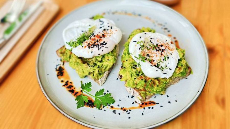 Delicious avocado toast featuring two poached eggs, elegantly presented on a white plate with a sprinkle of seasoning.