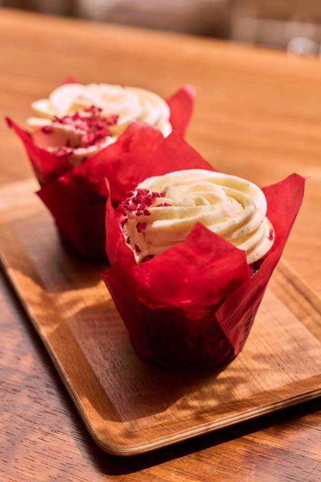 A wooden tray holds two red velvet cupcakes, adorned with luscious frosting, inviting a delightful treat.