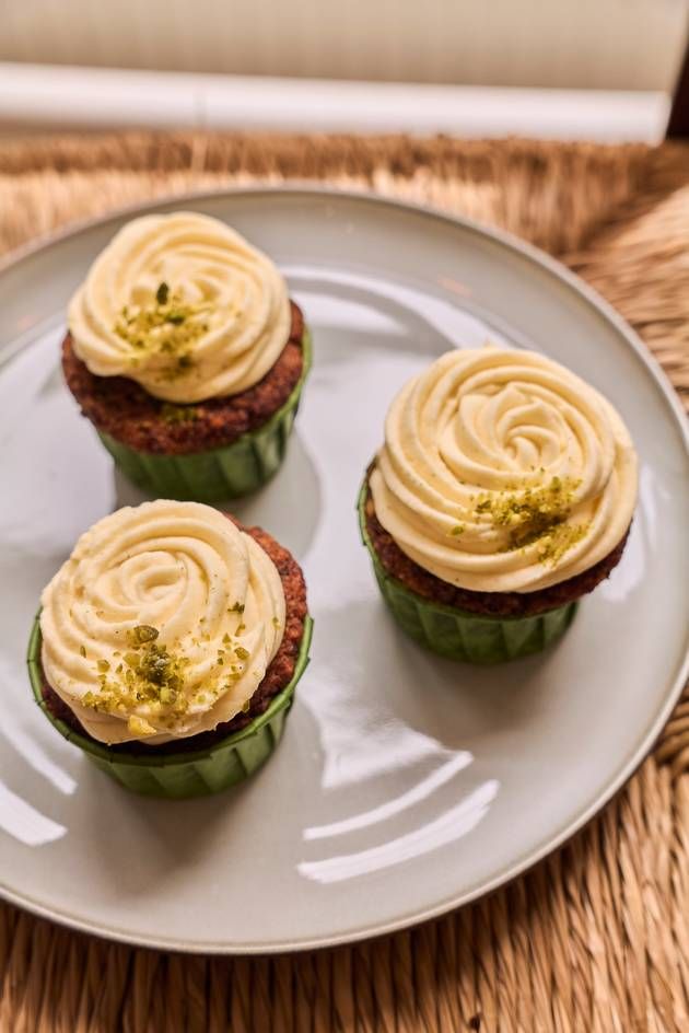 Three carrot cupcakes with cream frosting arranged on a decorative plate, showcasing their delightful appearance.