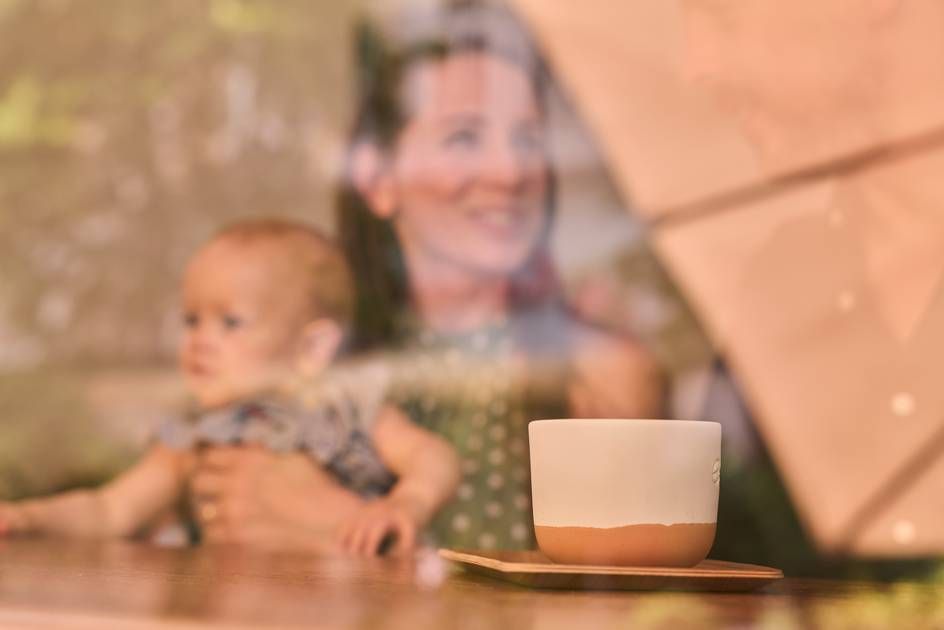 A coffee cup placed on a table with a view of a mother and child outside the window.