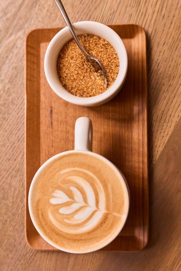 Espresso and brown sugar in two small coffee bowls and a spoon are neatly placed on a wooden tray, highlighting a charming coffee presentation.