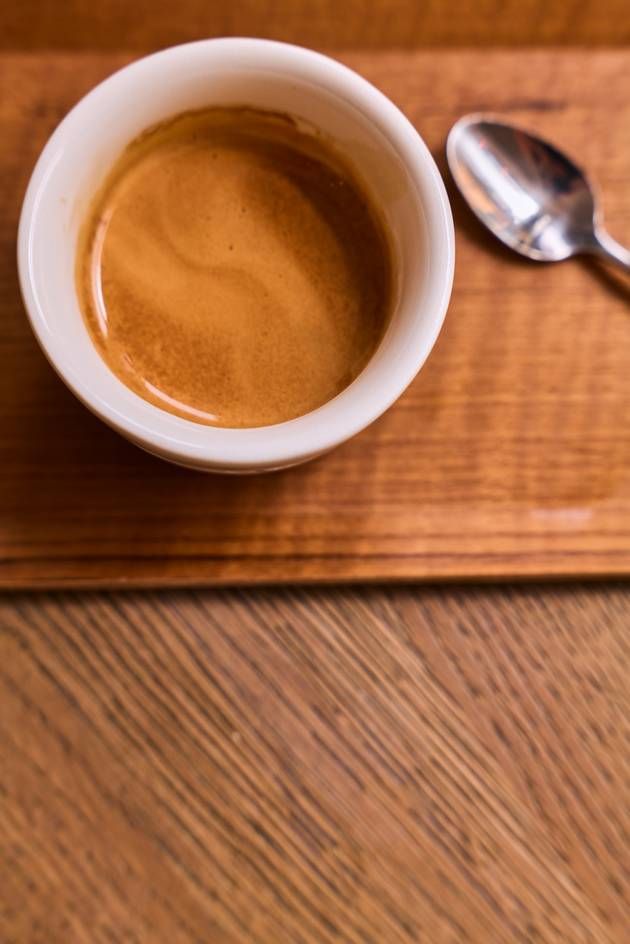 A small bowl of espresso sits on a rustic wooden table, showcasing its rich color and inviting aroma.