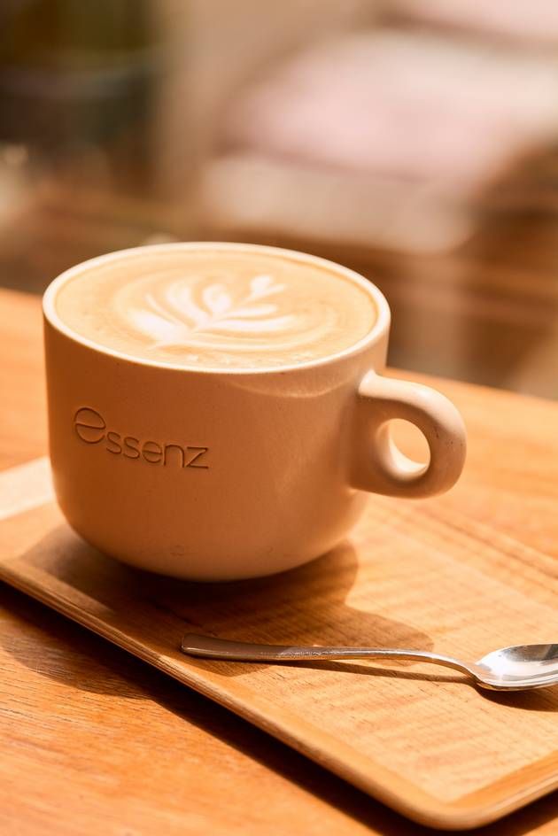 A beautifully crafted cup of Café Essenz coffee featuring art, resting on a natural wooden tray.