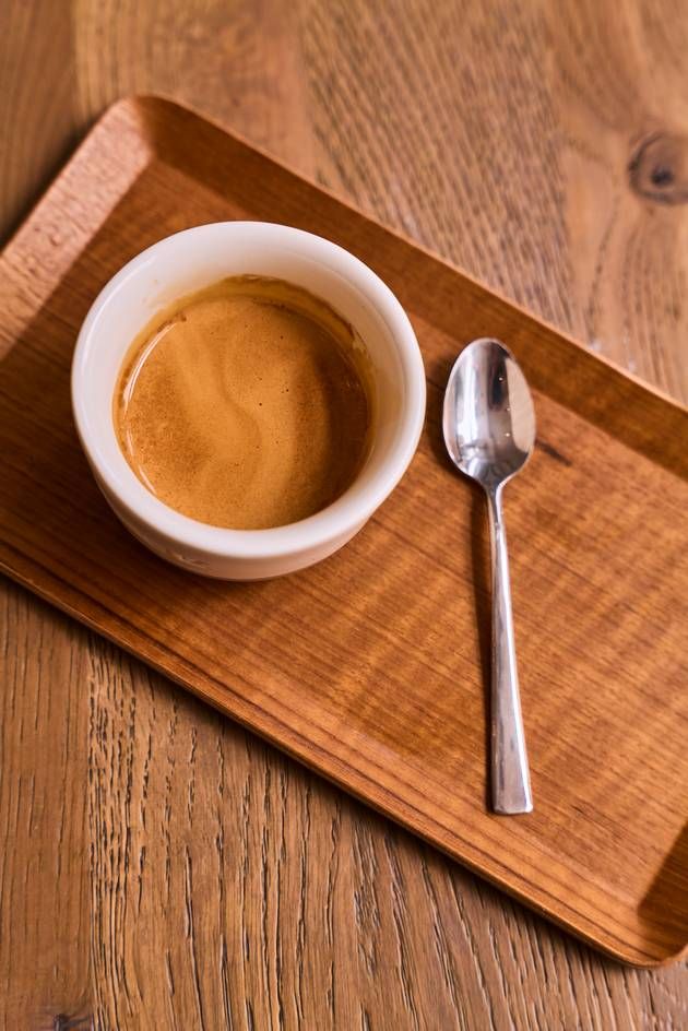 A cup of coffee and a spoon are elegantly placed on a wooden tray, showcasing a simple yet inviting coffee setup.