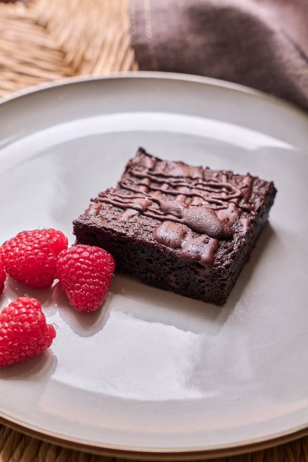 A delicious vegan brownie square on a plate, beautifully complemented by a handful of fresh raspberries.