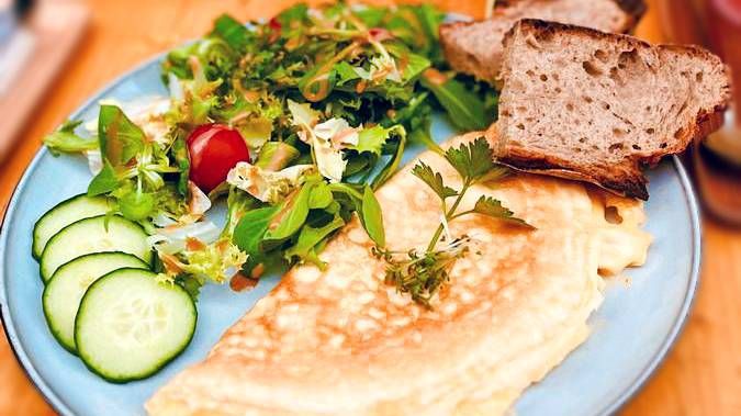 An appetizing omelette served on a blue plate, alongside bread, cucumber, and a vibrant salad.