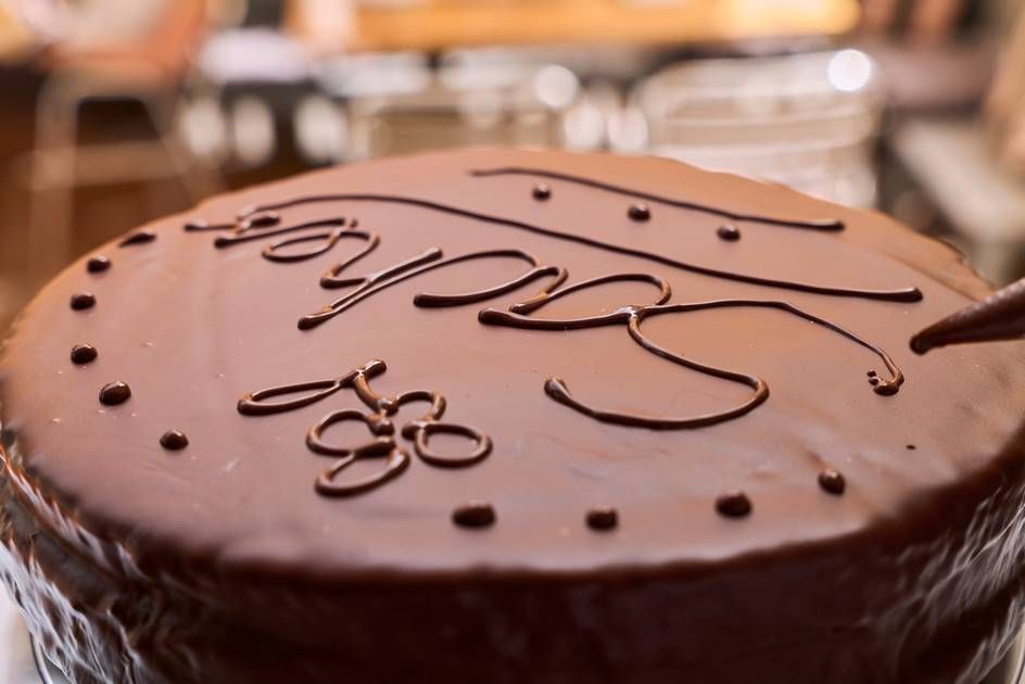 A luxurious chocolate cake with "chocolate" artistically written on it, representing the finishing touch of a Sacher Cake.