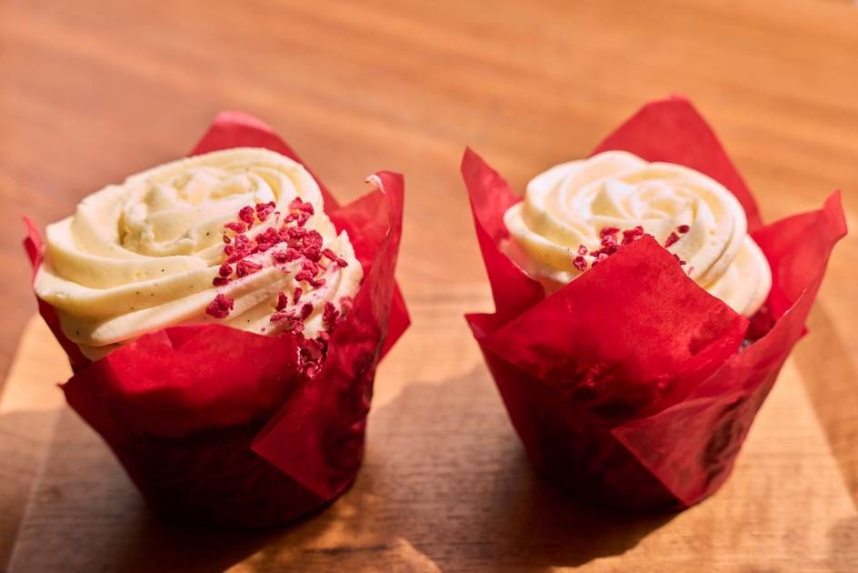 Two delicious red velvet cupcakes with red frosting, beautifully arranged on a wooden table surface.