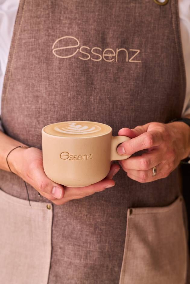 Barista holding a cup with coffee related drink at Café Essenz. Portrait view.