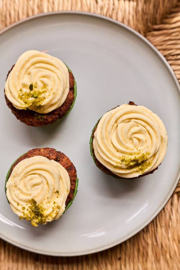 Three beautifully frosted carrot cupcakes on a plate, each adorned with creamy frosting, ready to be enjoyed.