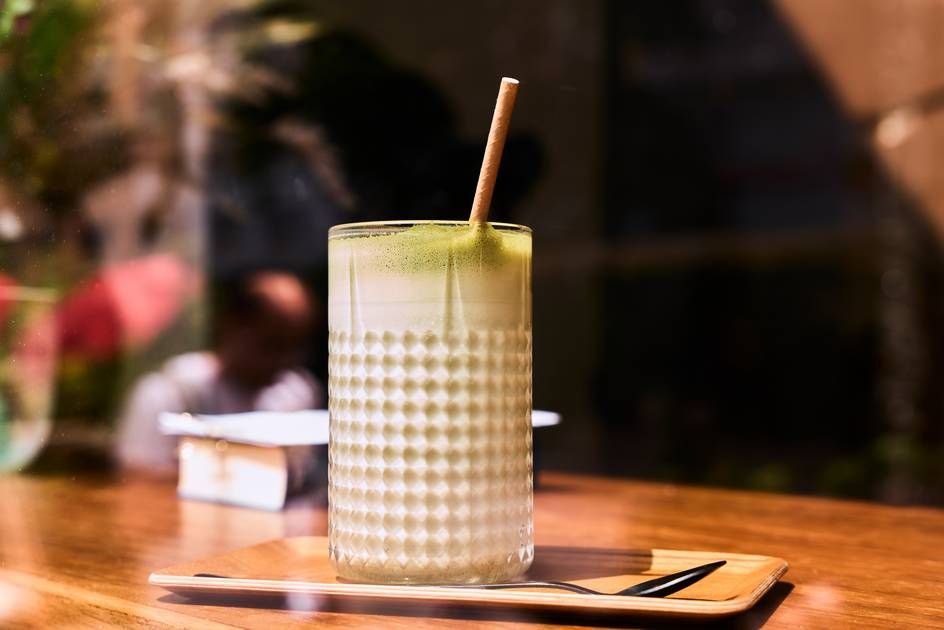 A chic glass of iced matcha latte with a straw, artfully positioned on a warm wooden table, exuding tranquility.